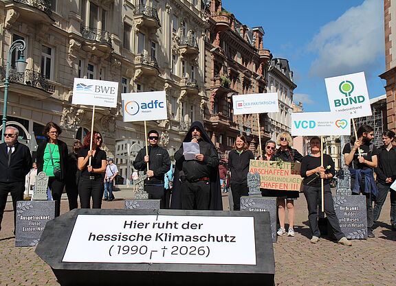 Menschen mit Schildern und Transparenten hinter einem Sarg, der die Aufschrift "Hier ruht der hessische Klimaschutz" trägt.