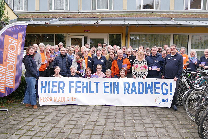Gruppenfoto 2 Die Gruppe der ADFC-Aktiven steht vor dem Eingang und hält ein Banner mit der Aufschrift „Hier fehlt ein Radweg“ in die Höhe
