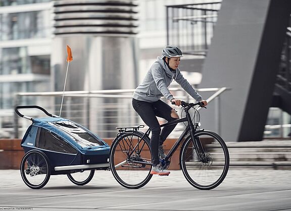 Eine Frau fährt auf einem Fahrrad mit einem Kinderanhänger.